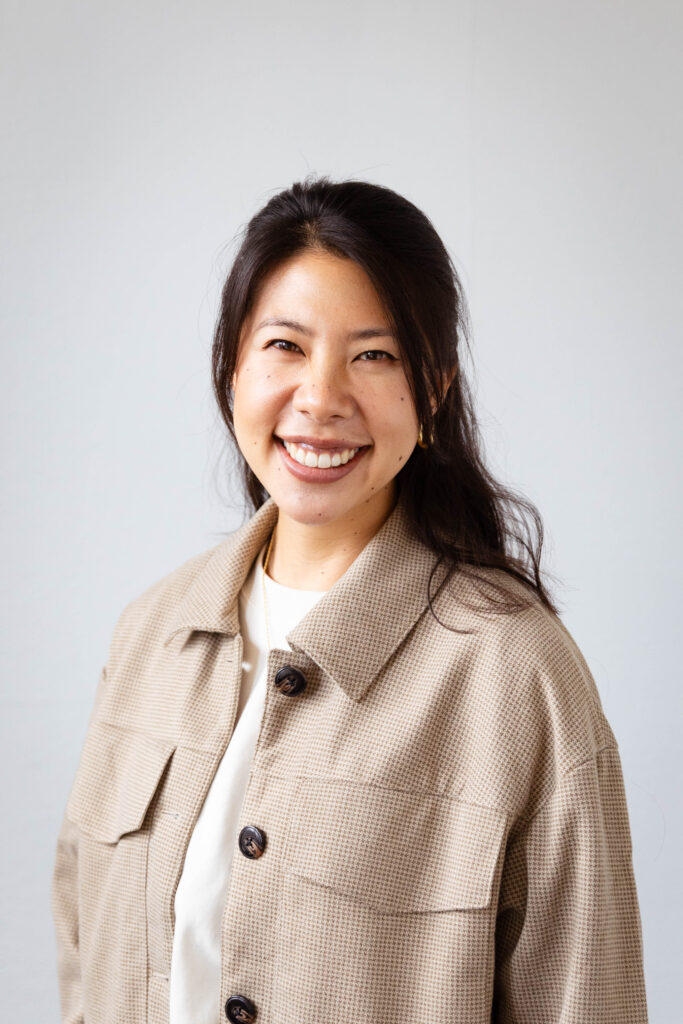 Young Asian American woman wearing a brown jacket and cream t shirt, smiling